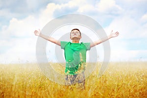 A boy standing in a field of wheat against cloudy photo