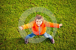 Boy standing on green grass with outstretched arms
