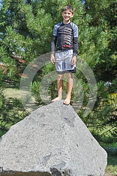 Boy Standing on a Large Rock by Pine Tree