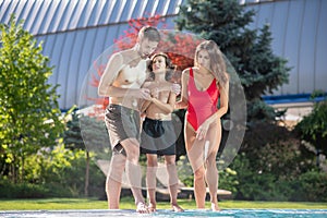 Boy standing near pool between his parents afraid of jumping into the water