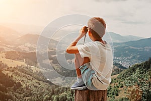 A Boy standing on of stump in summer mountains at sunset and enjoying view of nature