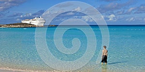 Boy standing on tropical beach with cruise ship