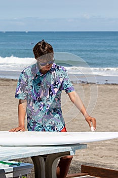 Boy standing waxing his surfboard, surf Japan