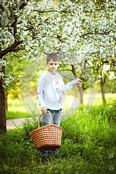 A boy stands in an apple orchard, holds a basket and looks straight