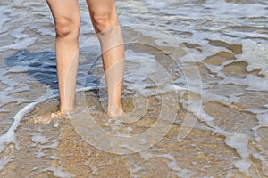 A boy stands on the beach and enjoys the waves on his legs