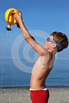 Boy stands on beach and pours sand watering-can