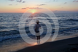 Boy stands on the beach at the sundown