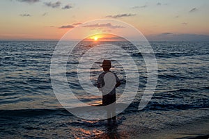 Boy stands on the beach at the sundown