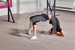 A boy stands in the bridge pose at the ballet school on the carpet.