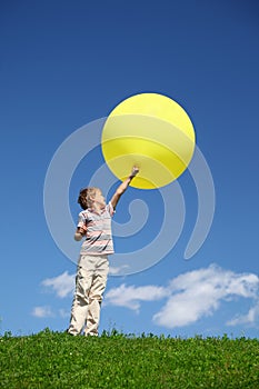 Boy stands in field and lifts balloon