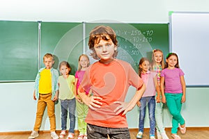 Boy stands in front of kids near blackboard