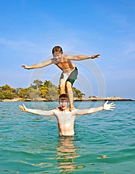 Boy stands on his brother's shoulders in an ocean bay