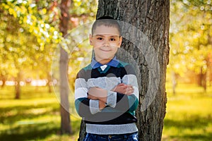 A boy stands leaning against a tree in a park