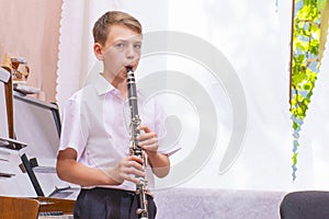 The boy stands near the window and plays on a black clarinet, looks at the camera. Musicology, music education and education.