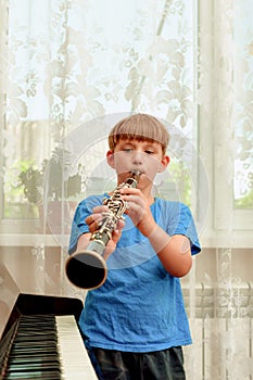 A boy stands next to the piano and plays the clarinet at a music school