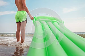 Boy stands on sea surf line with swimming air mattress