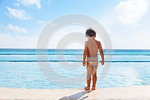 Boy stands on stone boarder of swimming pool