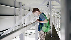 The boy stands under the bridge and look at the water. Walk under the bridge. Industrial landscape