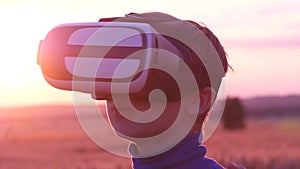 A boy stands in a wheat field at sunset in virtual glasses