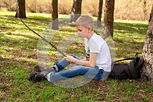 A boy with a stick sits on the grass in spring park