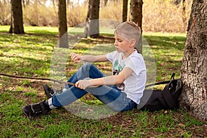 A boy with a stick sits on the grass in spring park