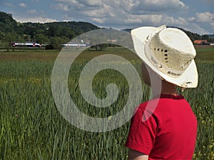 A boy in straw hat observing a train in the distance