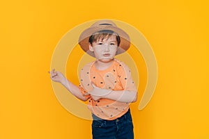 Boy in straw hat shows hands as opposite the yellow background with copyspace. Summer holiday concept
