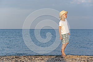 Boy in straw hat walks along the seashore in rays of sunset. Carelessness photo