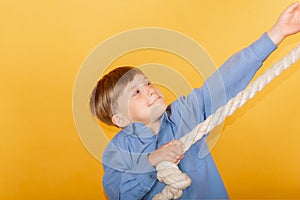 The boy stretches on a rope on a yellow background, the concept of achieving success