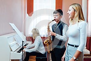 Boy student learns to play the saxophone in a music lesson to accompaniment of the piano