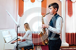 Boy student learns to play the saxophone in a music lesson to accompaniment of the piano