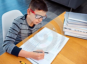 Boy, student and writing in book for math, studying or homework for learning, assessment or education on table. Smart