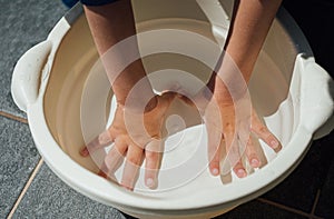 Boy submerging and washing his hands inside a basin with water.
