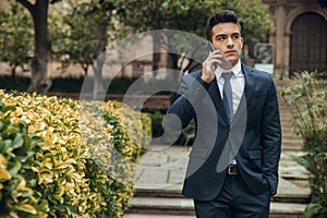 Boy in suit calling with phone and walking in park