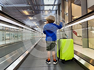 Boy with suitcase stands on a moving walkway at airport