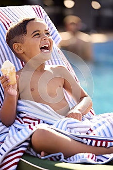 Boy On Summer Holiday On Lounger By Swimming Pool Eating Ice Cream