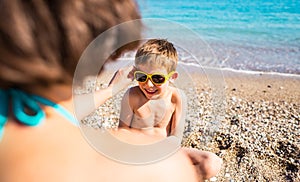 A boy in sunglasses plays on the beach