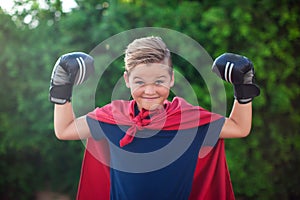 Boy superhero with boxing gloves and red cloak showing power outdoor. Childhood, success and and freedom concept