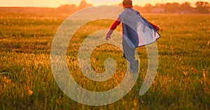 Boy in superhero costume and mask running across the field at sunset dreaming and fantasizing