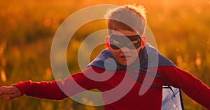 Boy in superhero costume and mask running across the field at sunset dreaming and fantasizing