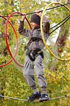 Boy surmounting obstacle course in the outdoor rope park among autumn foliage photo