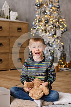 Boy in sweaters, sitting on wooden floor, plaing to toy bear