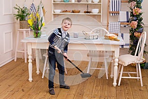 Boy sweeping the floor in the kitchen. Pretty boy helps parents