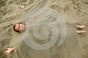 Boy after swimming is buried in sand on beach