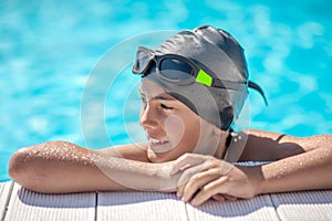 Boy in swimming cap resting his hands on poolside