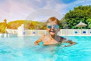 Boy with swimming goggles standing in outdoor pool