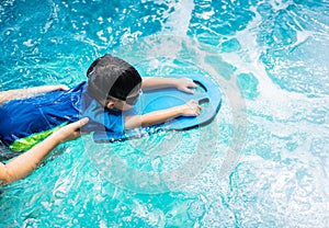 A boy is swimming with kickboard and swimming goggles