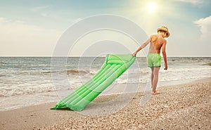 Boy with swimming mattress walks on sand sea beach