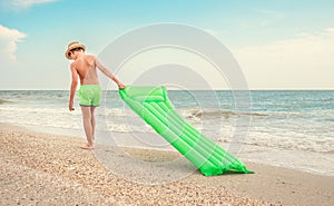 Boy with swimming mattress walks on sand sea beach