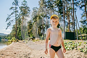 A boy in swimming trunks stands on the sandy shore